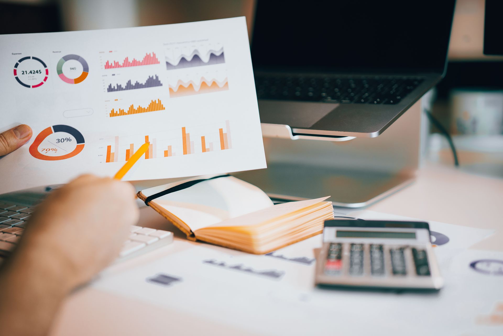Financial dashboard printout with revenue and expense donut charts above a desk with laptop and calculator