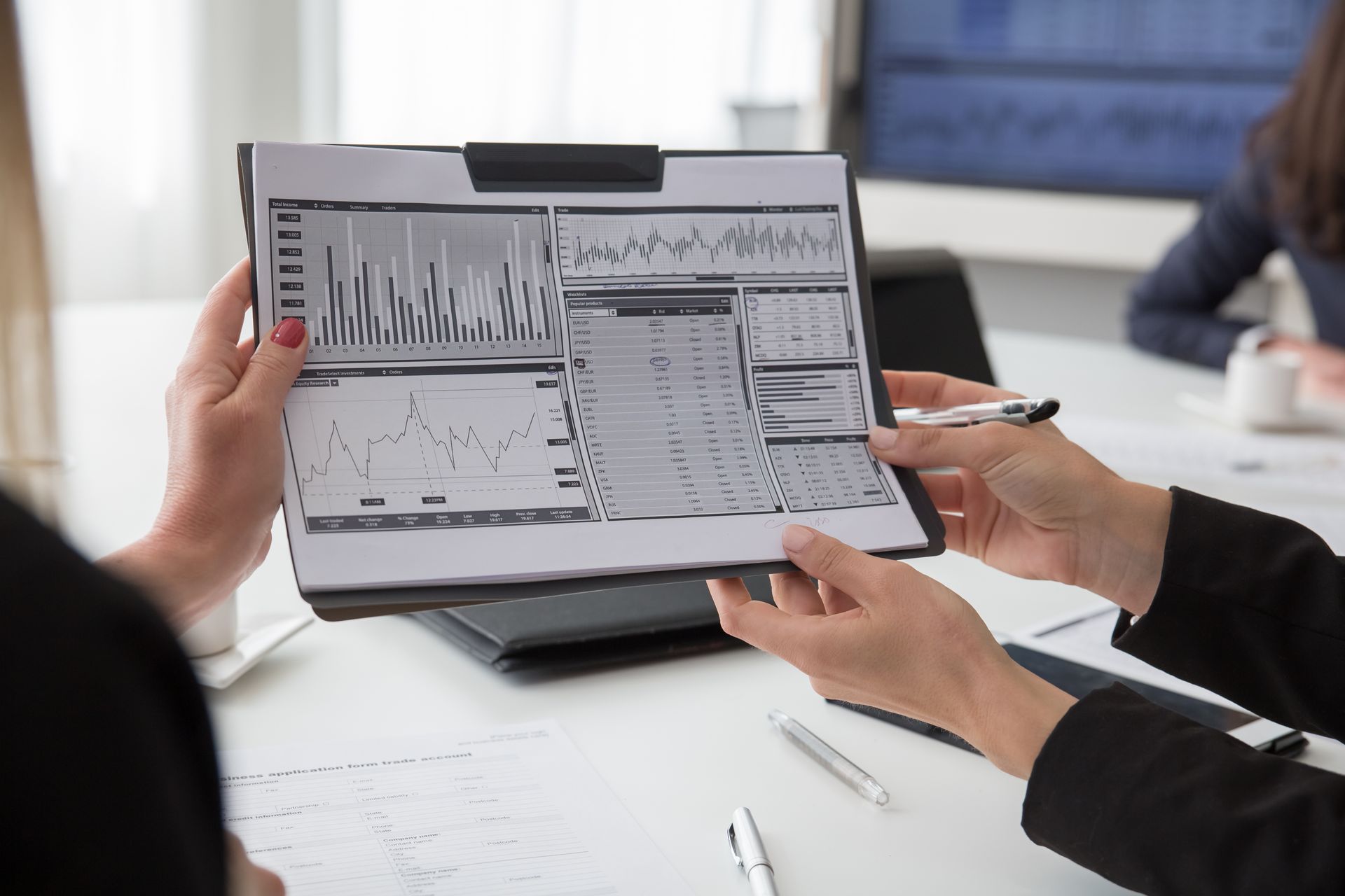 Two hands from opposite sides holding a printed multi-panel finance dashboard with bar chart and trend line